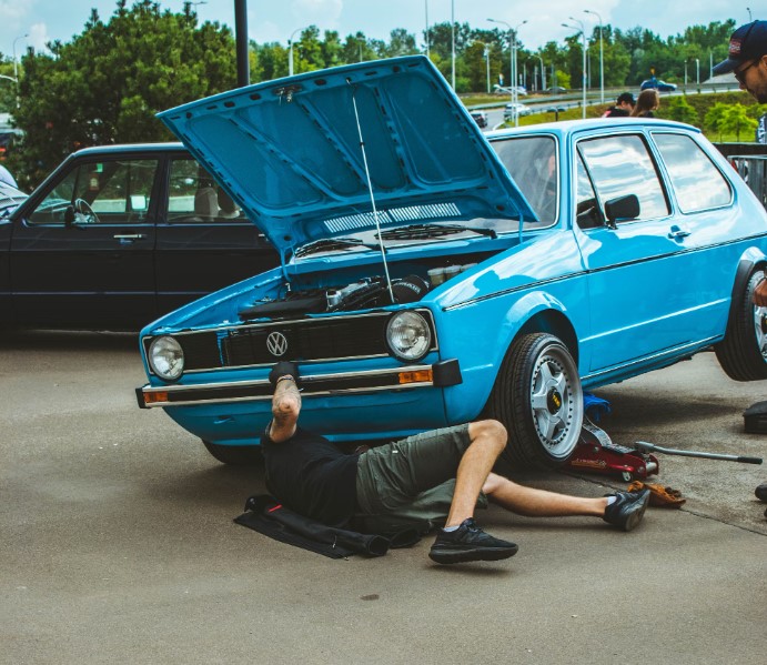 a-man-laying-on-the-ground-next-to-a-blue-car