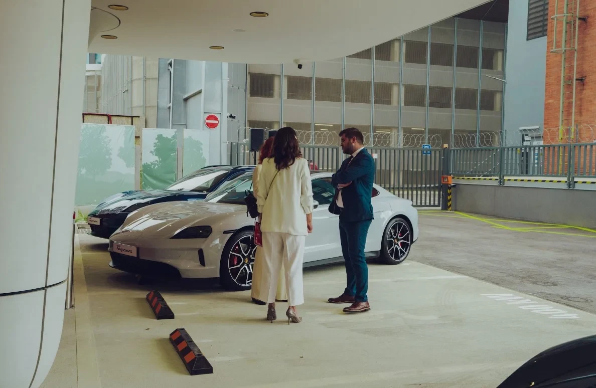 a-couple-of-women-standing-next-to-a-white-car.